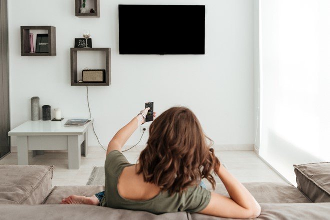 A tv hang on the wall with perfect height and a woman nis watching the tv