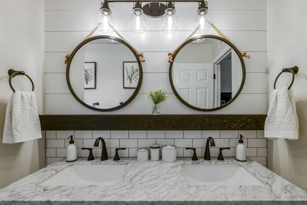 two circular mirrors in the washroom with towel, hand soap, basin