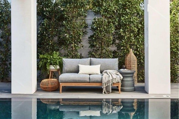 poolside silver color sofa set, trees, towels on the sofa and water in the pool.