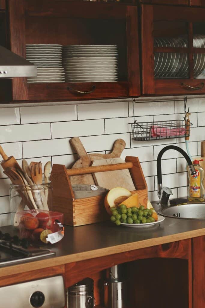 Rustic kitchen interior featuring a counter with fruits, wooden utensils, and a tiled backsplash.
