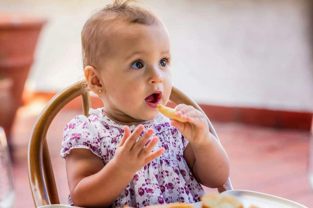 Cute baby girl in floral dress munching on a snack, enjoying a sunny day outside.