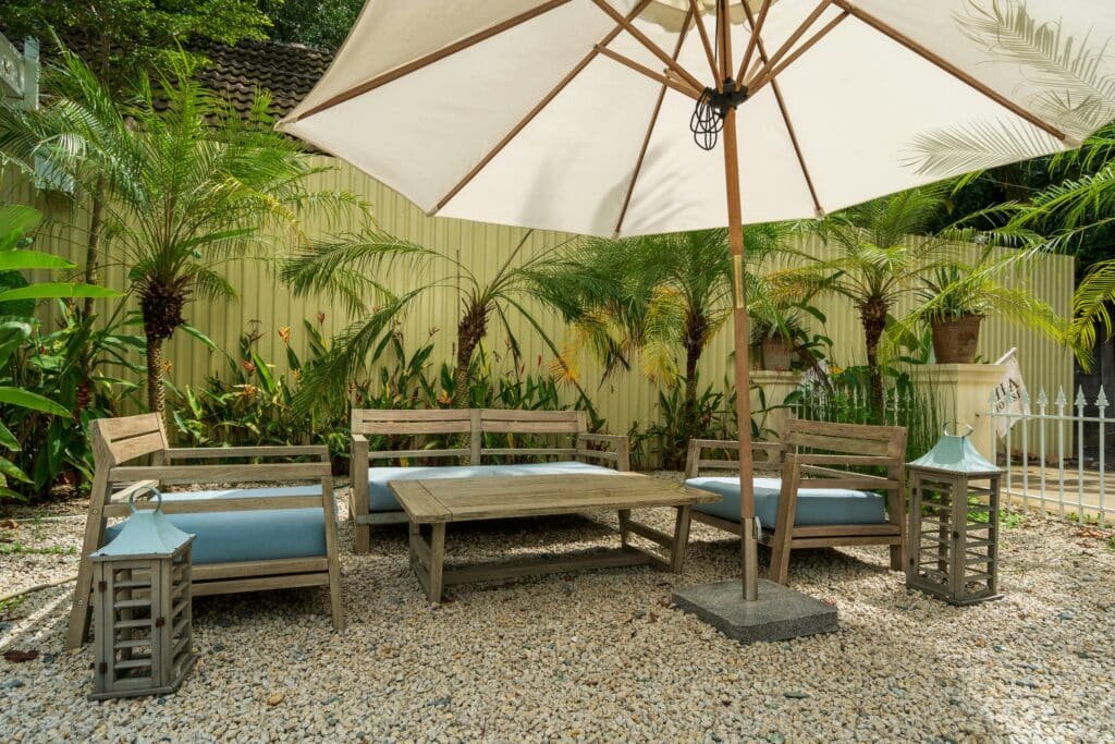 Cozy garden patio with wooden chairs, table, and umbrella surrounded by lush greenery.
