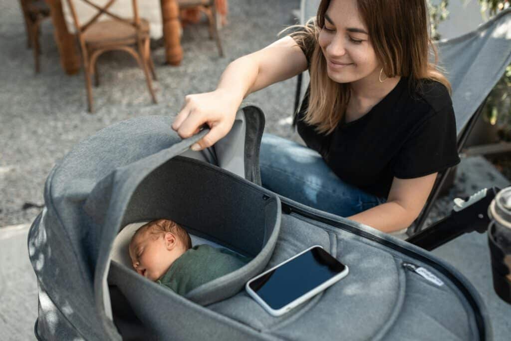 A mother joyfully gazing at her sleeping baby in a stroller, enjoying a sunny day.