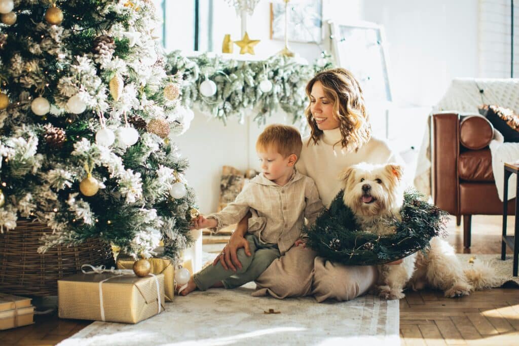 Mother and son decorating a Christmas tree with their dog, enjoying holiday togetherness.